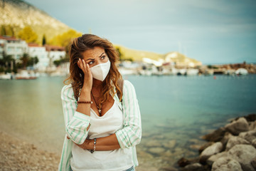 Fototapeta na wymiar Worried Young Woman With Protective Mask Thinking Of Something On The Beach
