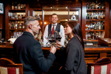 Cheers. Two casual business people in a hotel bar in the evening talking while having two glasses of red wine after check-in