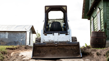 A skid steer loader clears the site for construction. Land work by the territory improvement. Machine for work in confined areas. Small tractor with a bucket for moving soil and bulk materials.