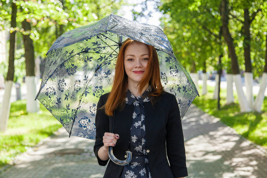 Red-haired girl with a lace umbrella walks along the green alley and laughs