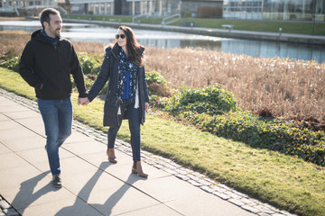 A young couple hold hands while talking and walking near a canal in the city of Edinburgh,...