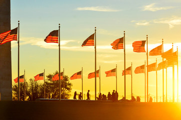 Washington Monument and silhouettes and waving national flags during sunset - Washington D.C....