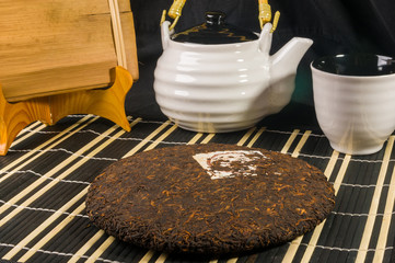 Chinese pressed PU-erh tea in bamboo leaf packaging and tea accessories on a bamboo Mat, close-up,...