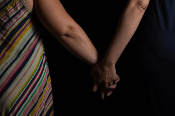 Young lesbian couple holding hands in studio with black background