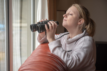 Women in late twenties spying with binoculars through s window