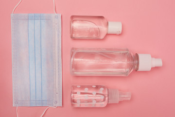 Top down view at flat lay of face mask and hand sanitizers on pink background, covid and PPE concept, copy space