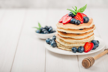 Classic american pancakes with fresh berry on white wood background. Summer homemade breakfast.