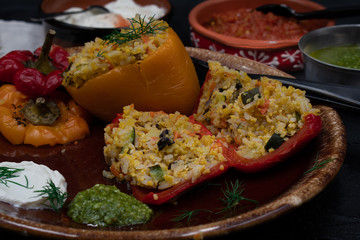 Vegan stuffed peppers with rice, corn grits, vegetables and herbs on clay servingware with side dishes