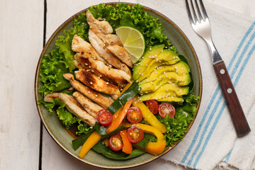 Grilled chicken salad with avocado and vegetables on white background