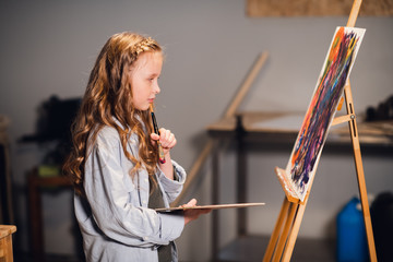 Young girl creative artist at work in a workshop. With passion draws a picture immersed in work