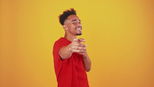 Happy african american guy dancing on orange studio background, flirting to camera