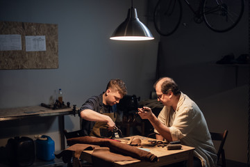 a respectable elderly shoemaker conducts a master class for a young boy on making shoes by hand in...