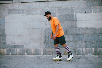 Handsome young stylish hipster guy with beard roller skating outdoors. Recreational activity. Aggressive roller skates