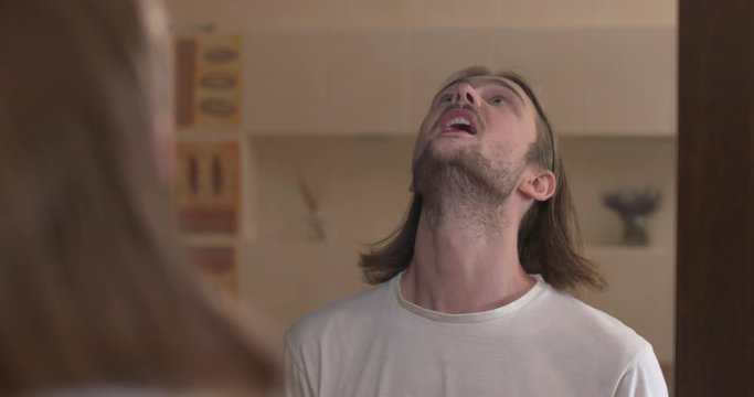 Young man stands in front of a mirror, gargle throat and spit out water