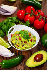 Bowl of Avocado Guacamole Mexican Dip with Avocado, Lime, Tomato, Cilantro with Fresh Ingredients with Tortilla Chips. Selective focus.