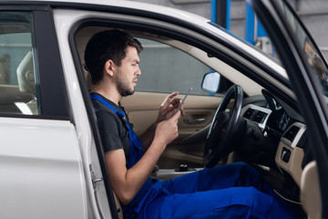 Car service worker sitting in a car in the front seat uses a telephone