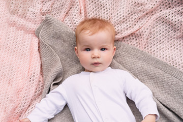  newborn baby in white clothes lies on  knitted blanket, view from above