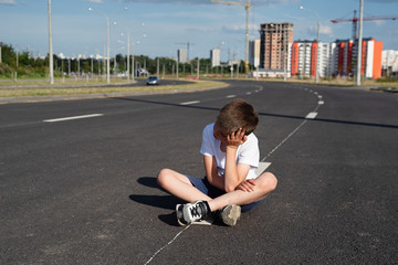 boy sits on  carriageway ,safety of children on  roadway, traffic rules concept, deadly threat