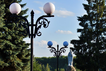 white lanterns lead to a religious monument among green firs