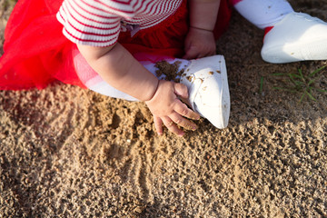 little girl in white tights and  red dress sits on  sand, touching  sand, view from above