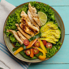 Grilled chicken salad with avocado and vegetables on turquoise background
