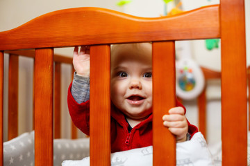 Obraz premium little child girl in a red sweater, smiles beautifully, in a crib, plays and has fun, emotional photo