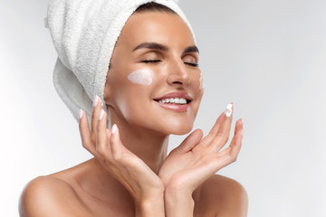 Close up of laughing half naked woman applying moisturizing face anti-aging cream on flawless skin, closed eyes, isolated on grey background. Natural makeup, anti age wrinkle serum. Beauty routine