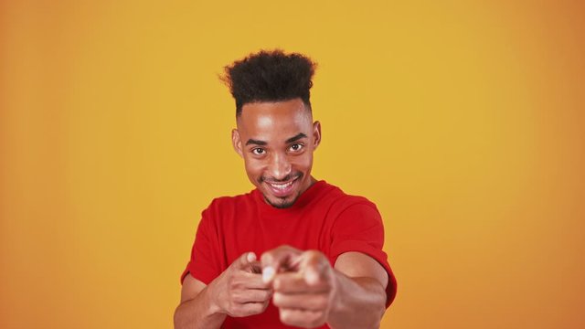 Cheerful black man jumping into shot and indicating happily at camera, orange studio background