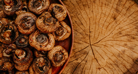 Cooked baked champignon mushrooms lie on a brown clay plate on a cracked brown hemp. Summer green blurred grass background.