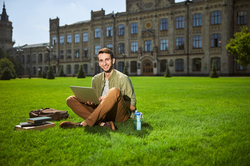 Obraz premium Good-looking merry dark-haired undergraduate with a laptop