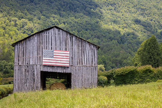 An old barn with an American flag painted somewhere in the mountains on a sunny day