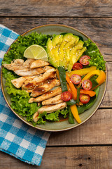 Grilled chicken salad with avocado and vegetables on wooden background
