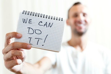 blurred man holds in his outstretched hand a sheet of paper with the inscription WE CAN DO IT