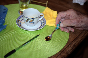 Old man hand holding coffee spoon over decorated table