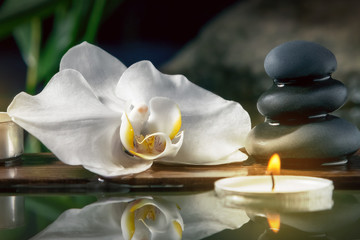 Black zen stones,candles and white orchids on a wooden plank on the surface of the water. SPA, relaxation, meditation concept