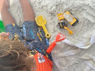 little boy playing on the beach with toys wearing sunglasses 