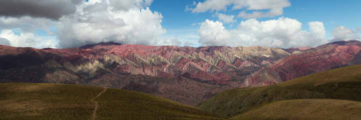 Geology. Andes mountain range. Panorama view of a footpath in the yellow grassland leading to the colorful Hornocal mountain under a dramatic cloudy sky in Humahuaca, Jujuy, Argentina. 