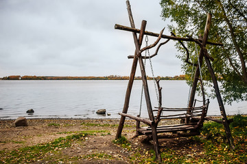 Fototapeta na wymiar Wooden swing on lake by autumn cloudy day