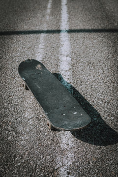 Vertical shot of an old black skateboard on the concrete ground