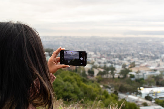 Cityscape view from a hill in San Francisco, CA with a girl holding a cell phone taking a photo