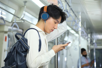 A lifestyle of young Asian man using cellphone with headset while taking the subway train to work...