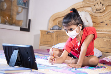 Little girl kid student wearing mask studying online class with tablet at home, New normal.Covid-19 coronavirus.Social distancing, home schooling.