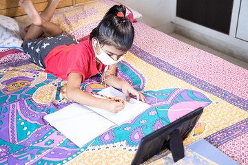Little girl kid student wearing mask studying with tablet at home, Distance learning online education.Covid-19 coronavirus.Social distancing, home schooling. omicron cases 