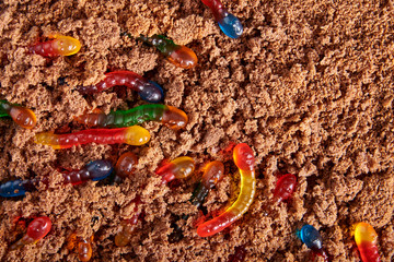 Colorful and bright assorted gummy worms in chocolate cake ground