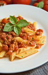 Penne  bolognese with basil leaf on white plate.
