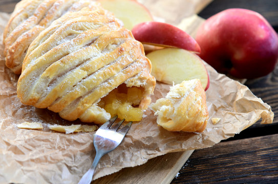 Easy Apple Turnovers (German name is Apfeltaschen) on brown paper with fresh red apples on wooden board and wooden floor.