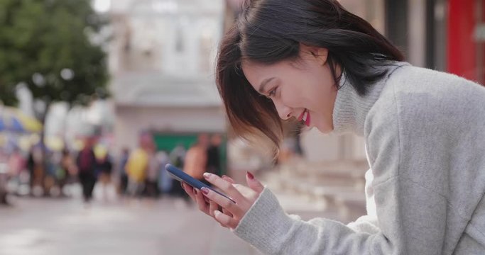 Side view of happy young asian woman using mobile phone browsing social medial in the urban street with people walking in the background  at Chengdu Sichuan China 
