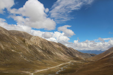 View of mountains, dirt road and stream with the dramatic sky in Tibet, China