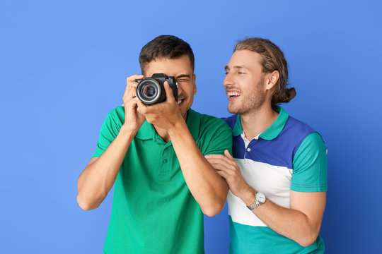 Happy gay couple with photo camera on color background