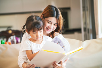 Asian mother reading book to her daughter at home during home schooling